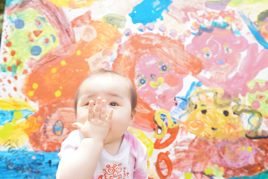 鮮やかな暖色の絵の前でポーズをとる赤ちゃん