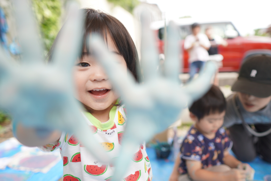 カメラに向かって、絵の具のついた手を広げる子供